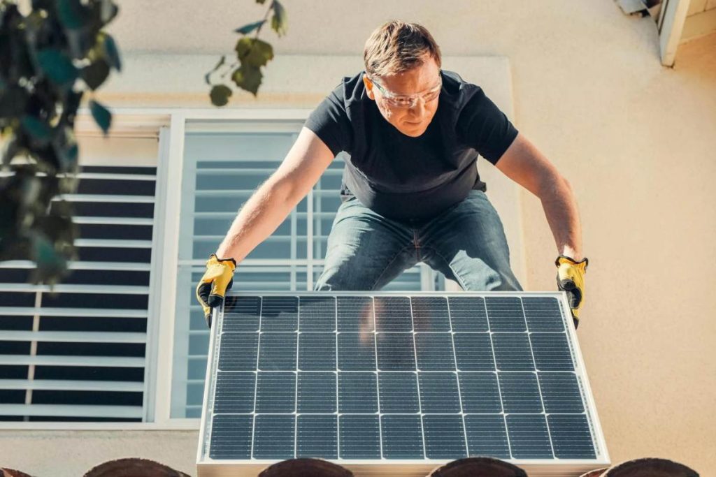 A man holding a solar panel in his hands while on the roof